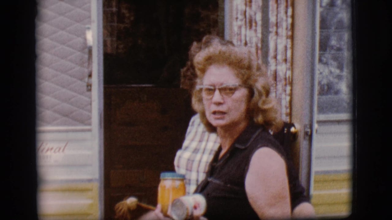 Woman with glasses holding a jar or can outside a mobile home doorway.