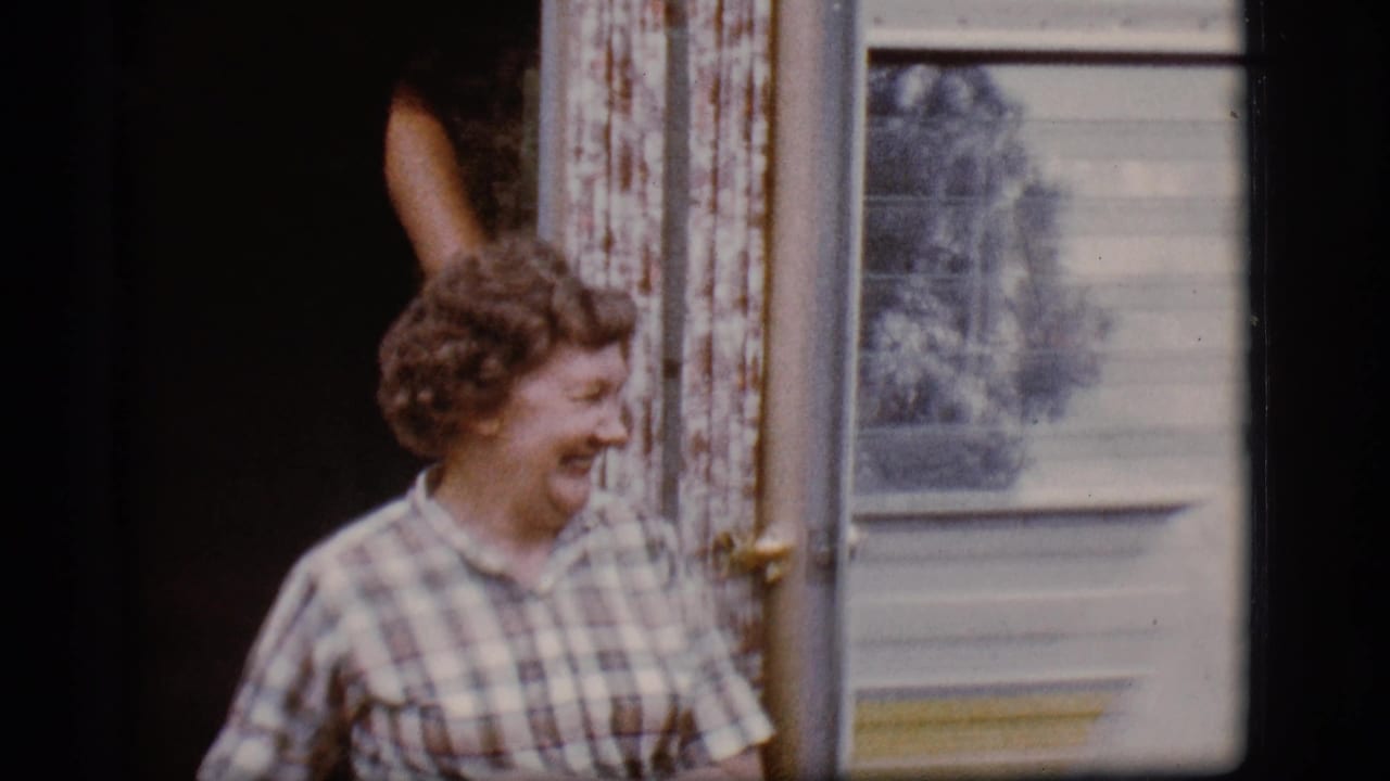 Woman in a plaid shirt laughs beside an open yellow-and-white camper door.