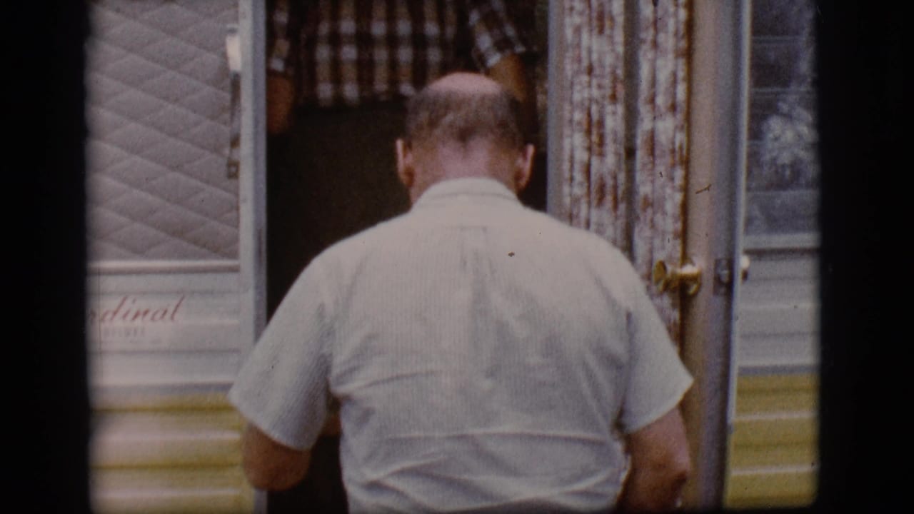 Balding man seen from behind entering a vintage travel trailer.