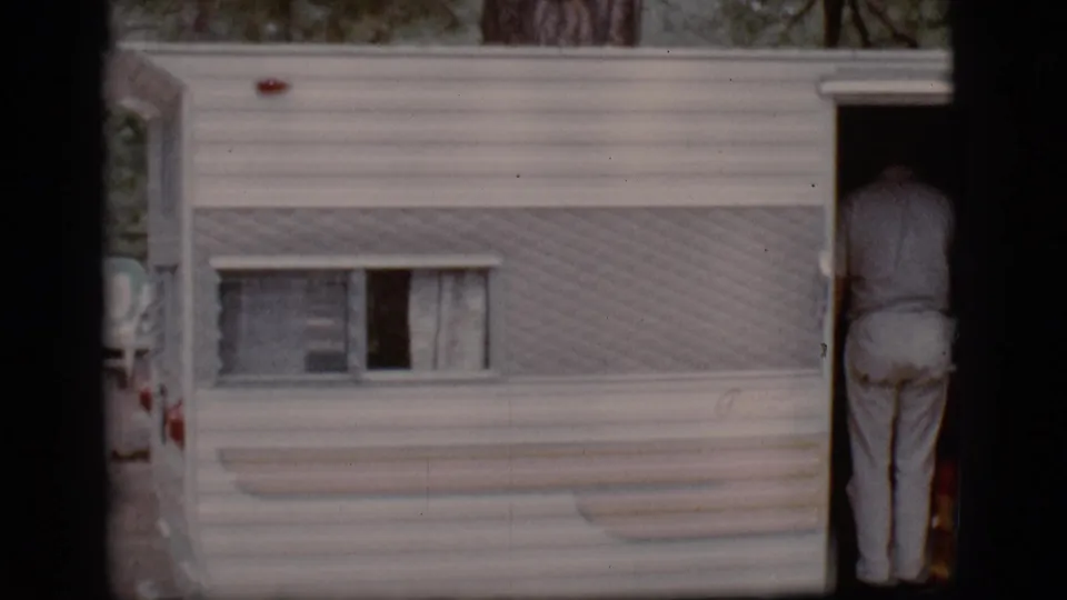 1968 Flagstaff campground view of a white camper trailer as a person in light clothing stands in the open doorway.