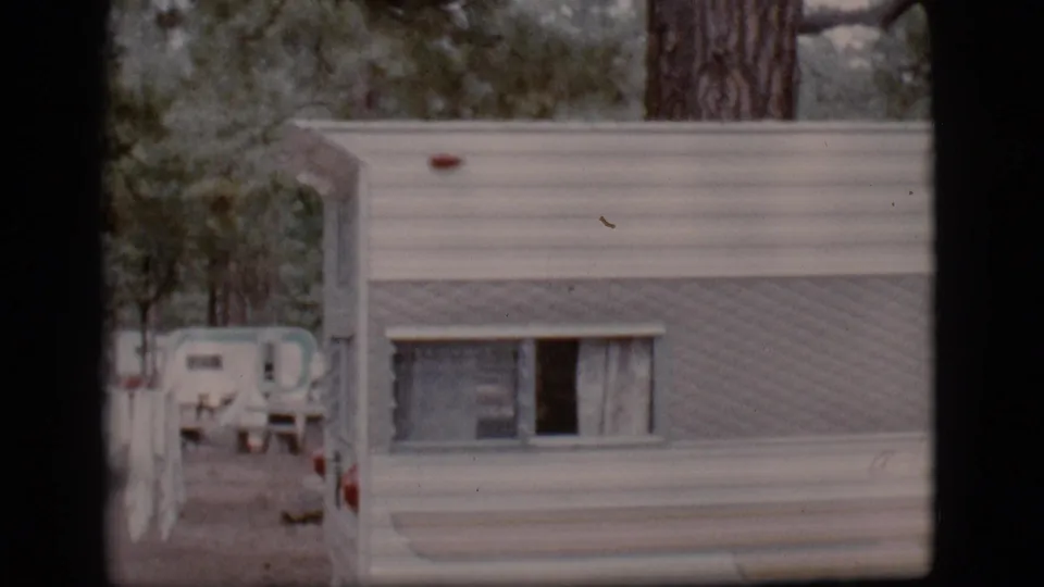 White camper trailer parked in a wooded Flagstaff campground, with another trailer visible down the road.