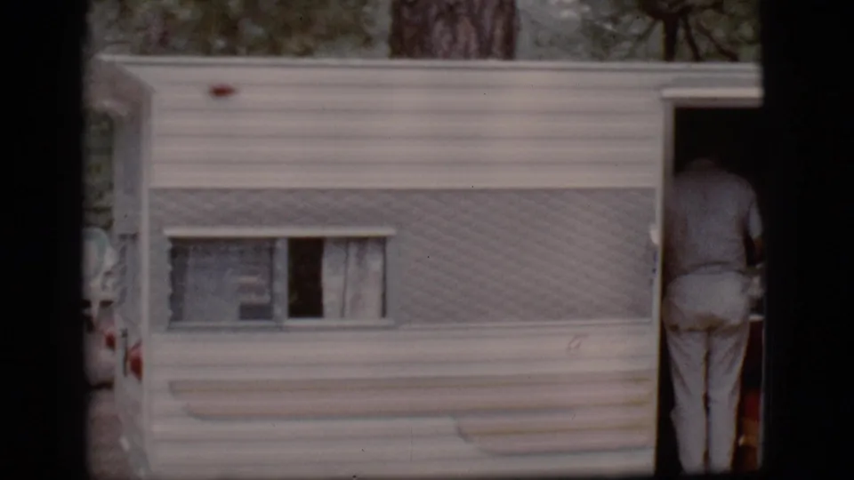 A person in light clothing is partly visible at the open doorway of a white camper trailer in Flagstaff, 1968.