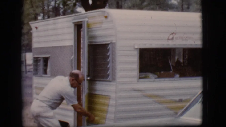 At the end of the Flagstaff campsite clip, the man bends near the open camper entrance beside the yellow-and-white trailer.