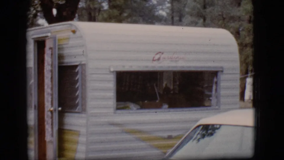 Side view of the white camper trailer at the wooded Flagstaff campsite, showing its open door and large window.