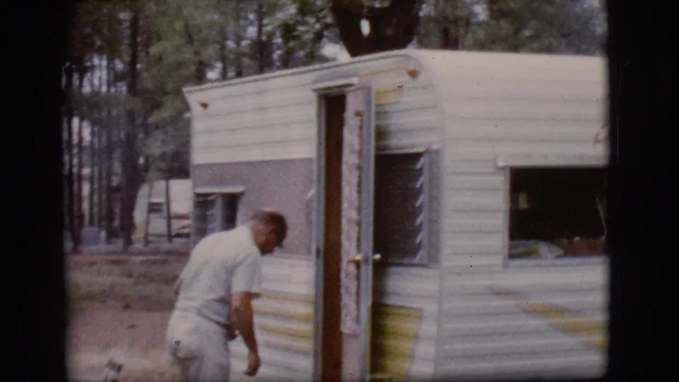 Adult man in light clothing stands by the open door of a white camper trailer in Flagstaff, Arizona, in 1968.