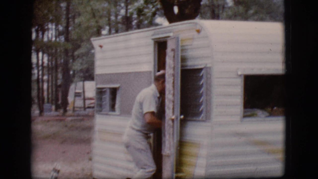 The man enters the open door of the small camper trailer in wooded 1968 Flagstaff campsite footage.