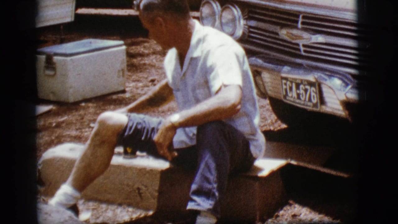 Man seated on a concrete block beside a Chevrolet front end and white cooler.