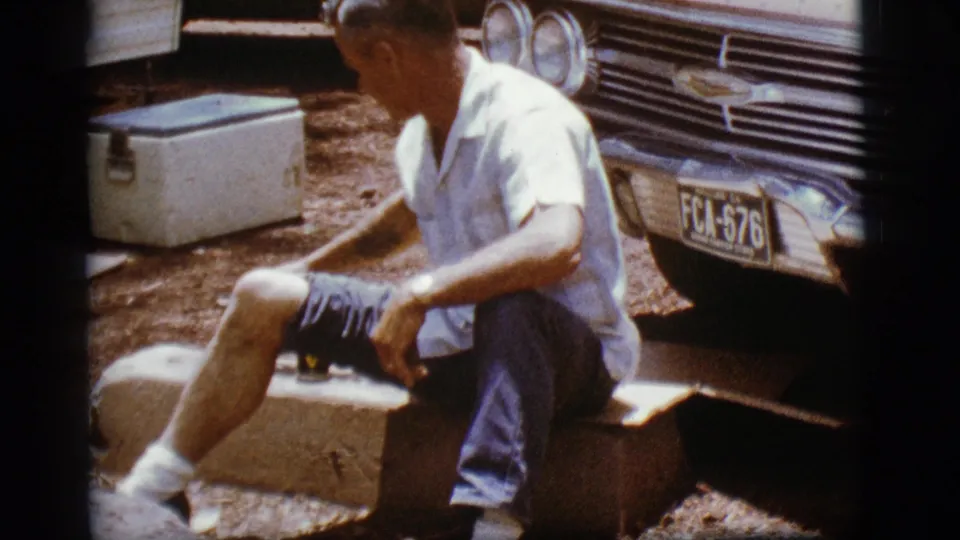 In 1968 Flagstaff home-movie footage, an adult man sits beside a vintage Chevrolet with a white cooler nearby.