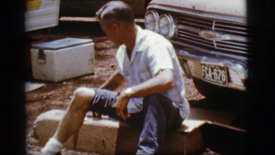An adult man in a white shirt sits outdoors beside a 1960s Chevrolet and cooler in Flagstaff, Arizona.