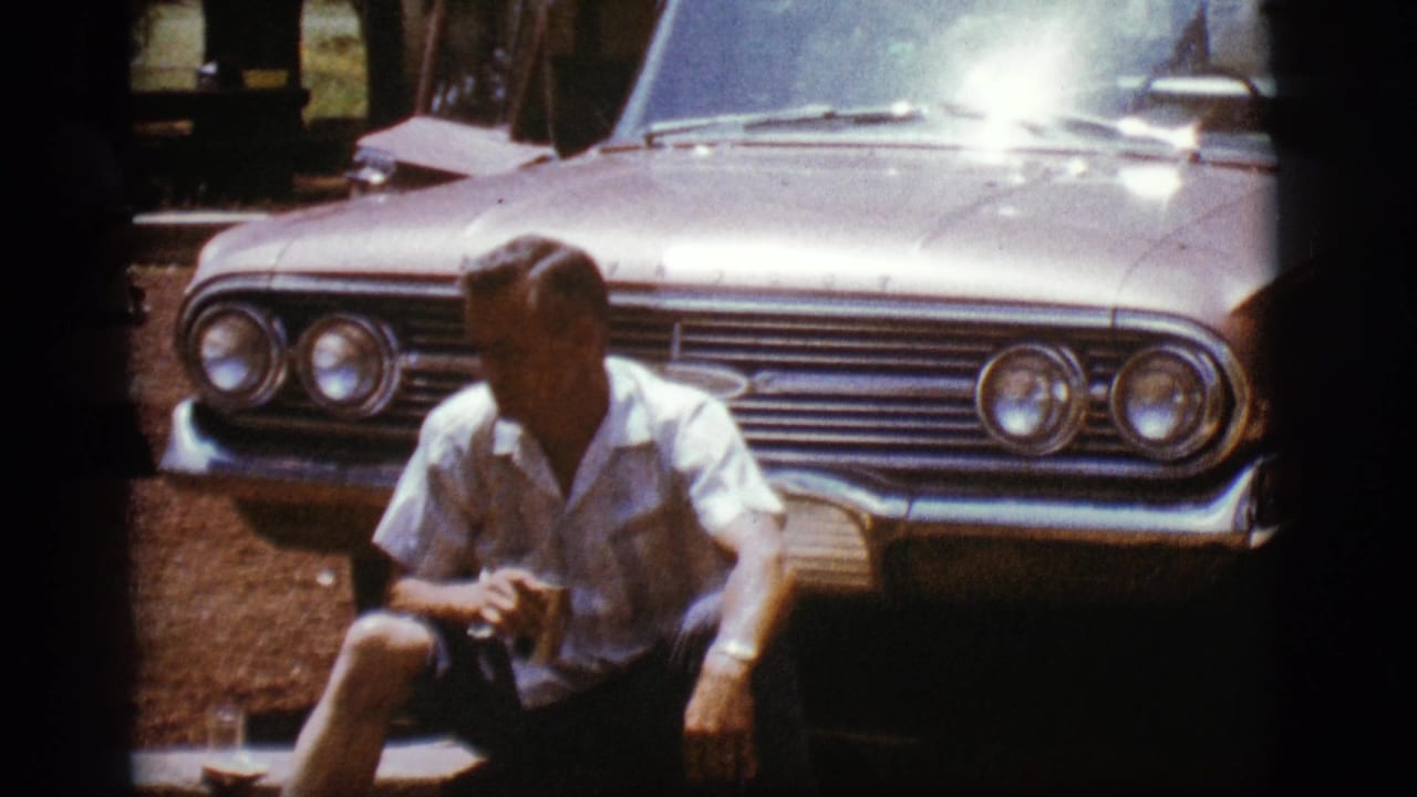 Seated man holds a can in front of a sunlit vintage Chevrolet grille.