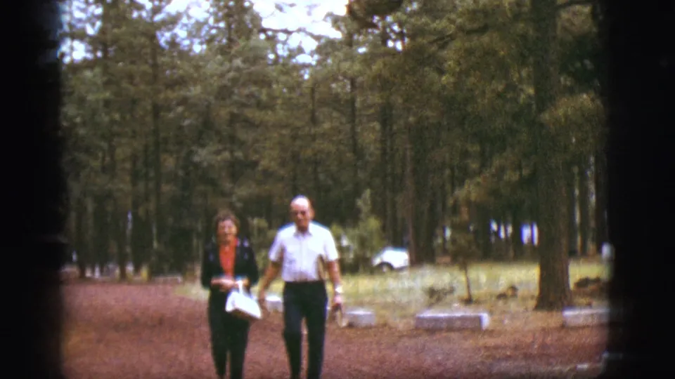 Older couple walking toward the camera on a wooded path in Flagstaff, Arizona, from supplied 1968 8mm footage.