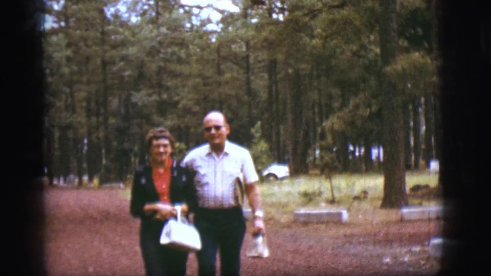 Older couple smiles near the camera on a pine-lined path in the supplied Flagstaff, Arizona 1968 footage.