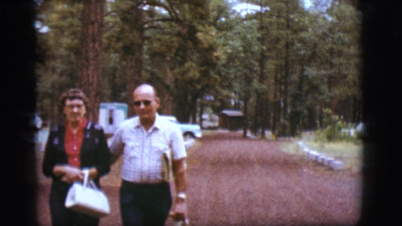Adult couple walking together on a wooded path with trailers behind them.