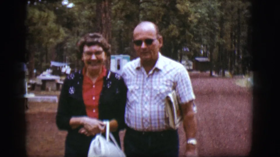Near the end of the clip, the couple fills more of the frame on the wooded path, with trailers and trees still visible behind them.