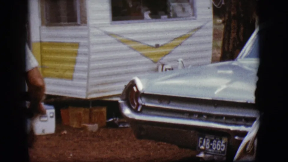 A turquoise car with chrome trim sits beside a white-and-yellow trailer at the wooded Flagstaff campground.
