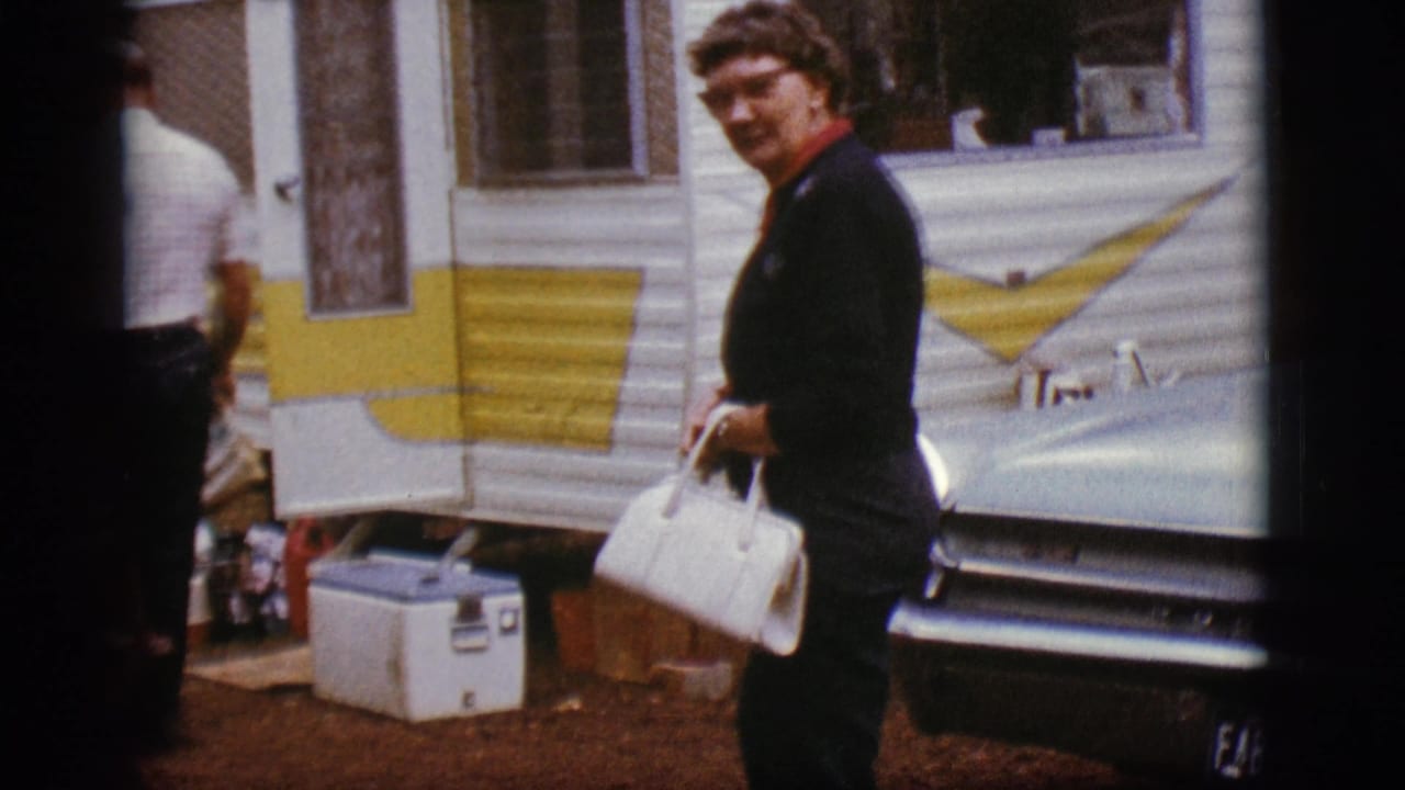 A woman in dark clothing carries a white handbag near a white and yellow camper trailer and classic car in Flagstaff, Arizona.