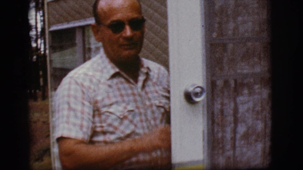 Man in sunglasses and plaid shirt standing beside a camper trailer door.