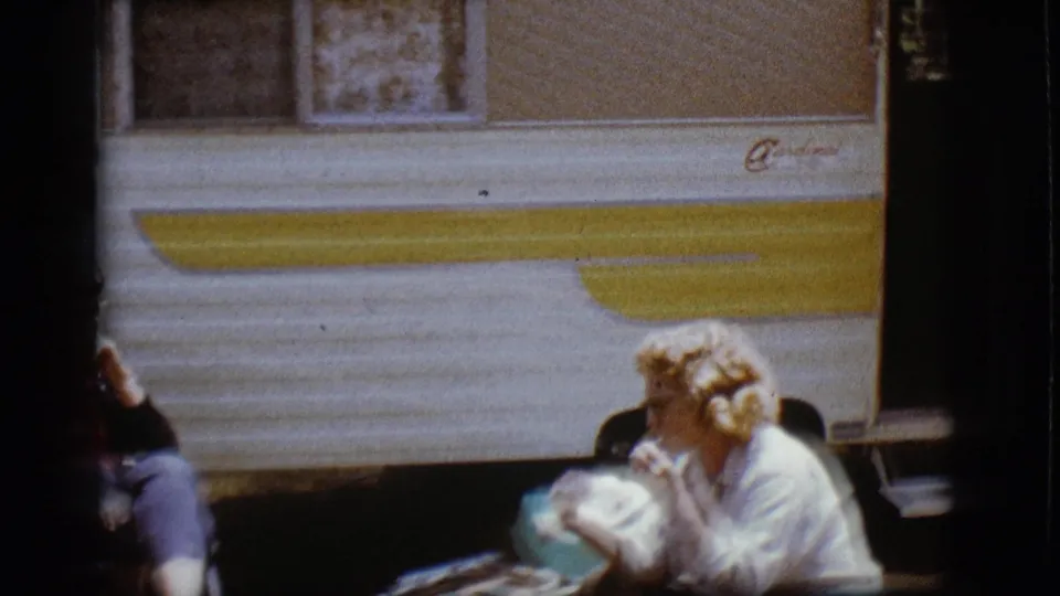 A 1968 Flagstaff home-movie frame shows two women outside the Cardinal RV during a casual meal break.