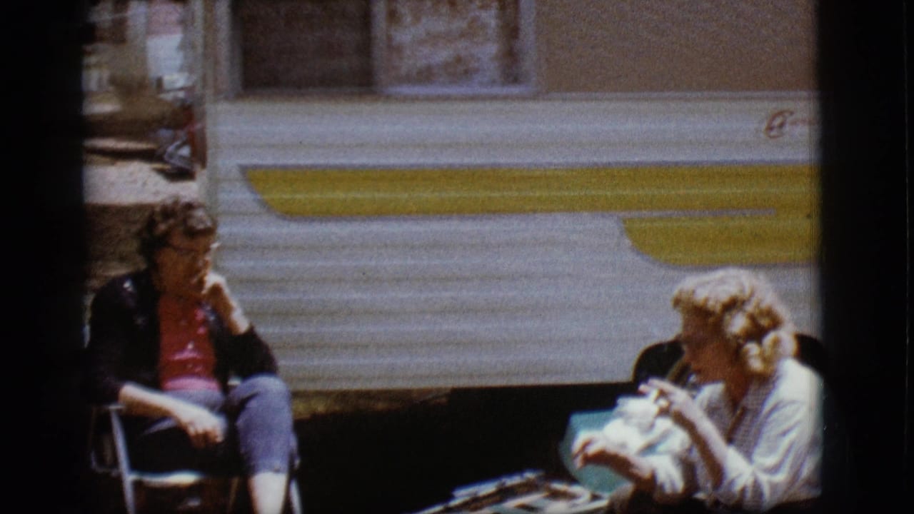 Two women sit in folding chairs beside a white and yellow trailer.