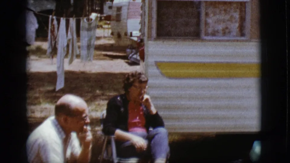 A man and woman remain seated outside the white and yellow trailer in this 1968 Flagstaff home-movie frame.