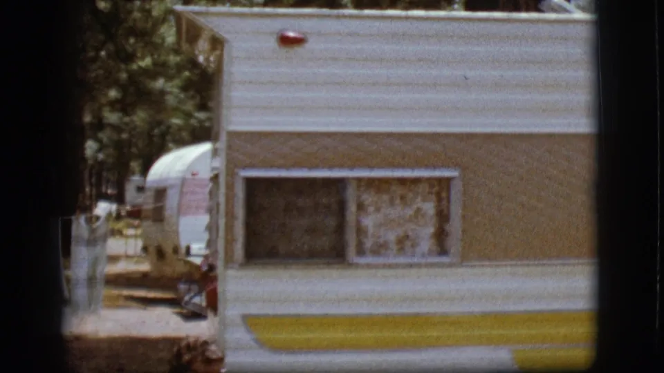 White and yellow camper at a wooded Flagstaff campground, with laundry on a line and another trailer behind it.