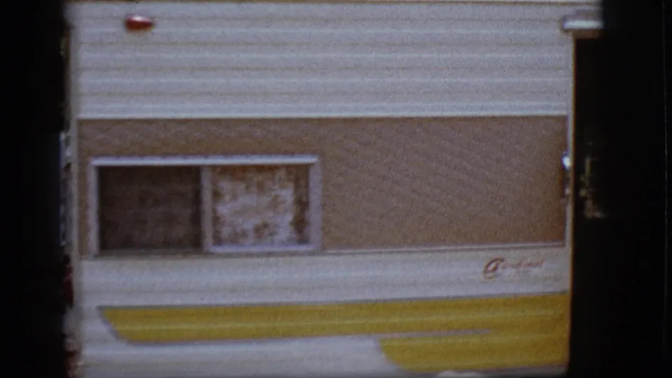 Close 8mm view of a Cardinal camper side, showing curtained windows and yellow trim in a campground setting.