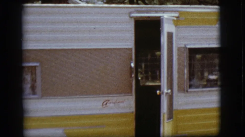White and yellow camper with an open door and side window, seen in 1968 campground home-movie footage.