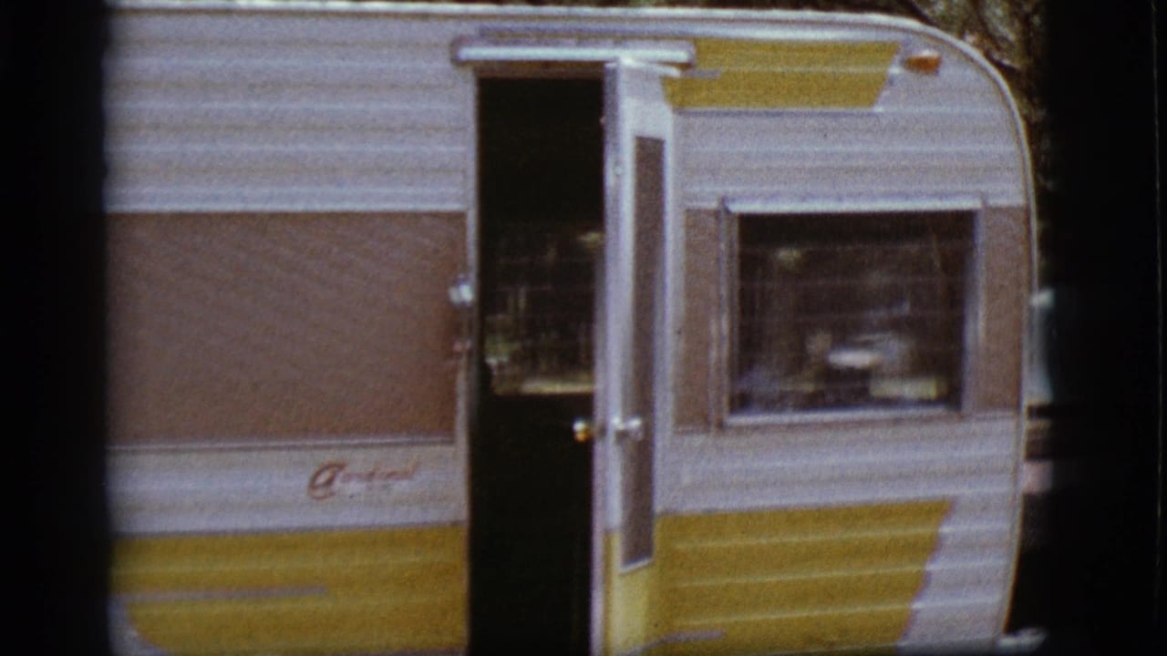 Yellow, brown, and white camper trailer with an open side door at a wooded campground.