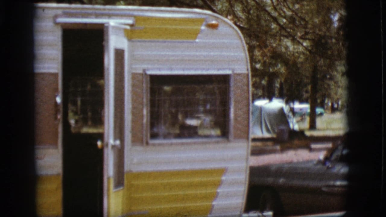 1968 Flagstaff home-movie frame showing the camper door and window, with trees, a tent, and a vintage car nearby.