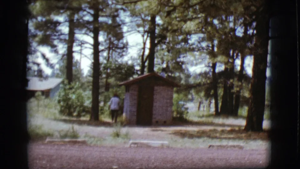 Late-clip frame from 1968 near Flagstaff with a woman walking past a small shed among pine trees.