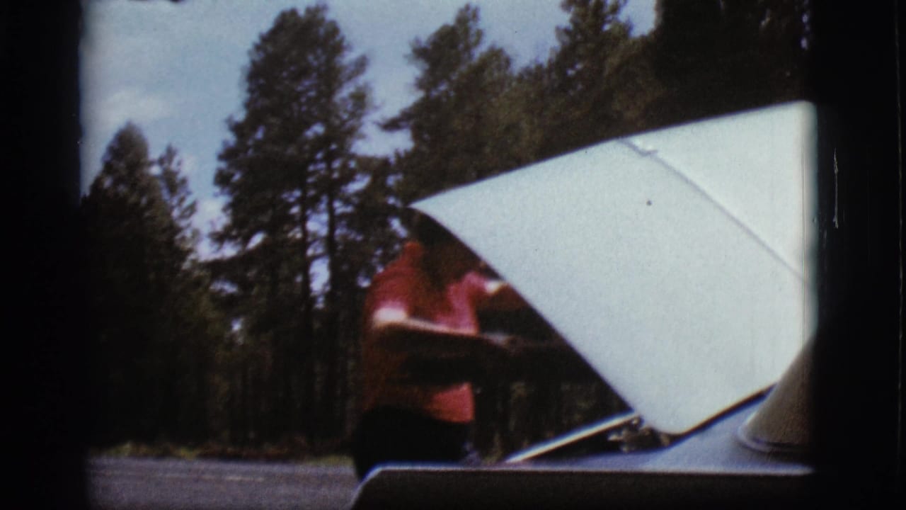 A man in a red shirt stands partly behind the raised hood of a parked car in 1968 Flagstaff forest footage.