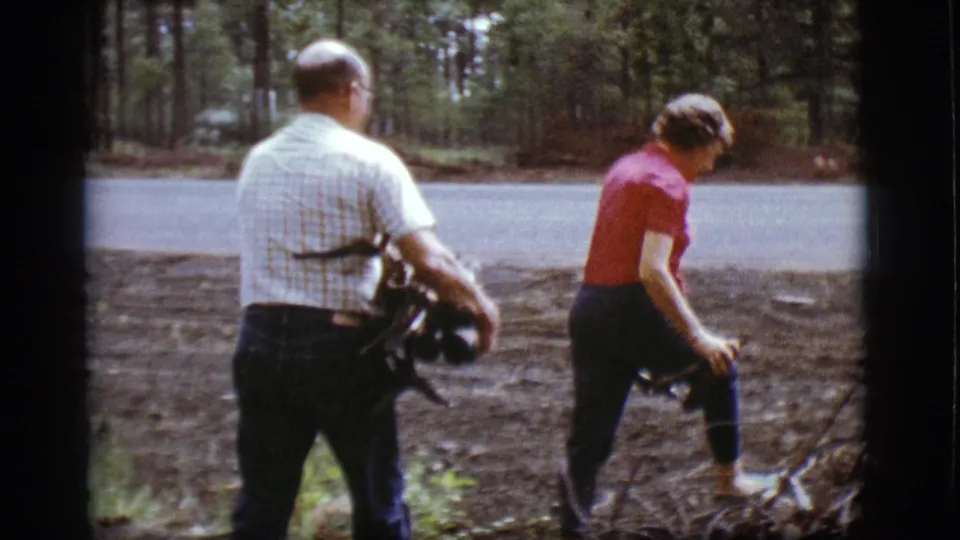 The woman steps through the wooded shoulder while the man carries a bundle of kindling near the Flagstaff road.