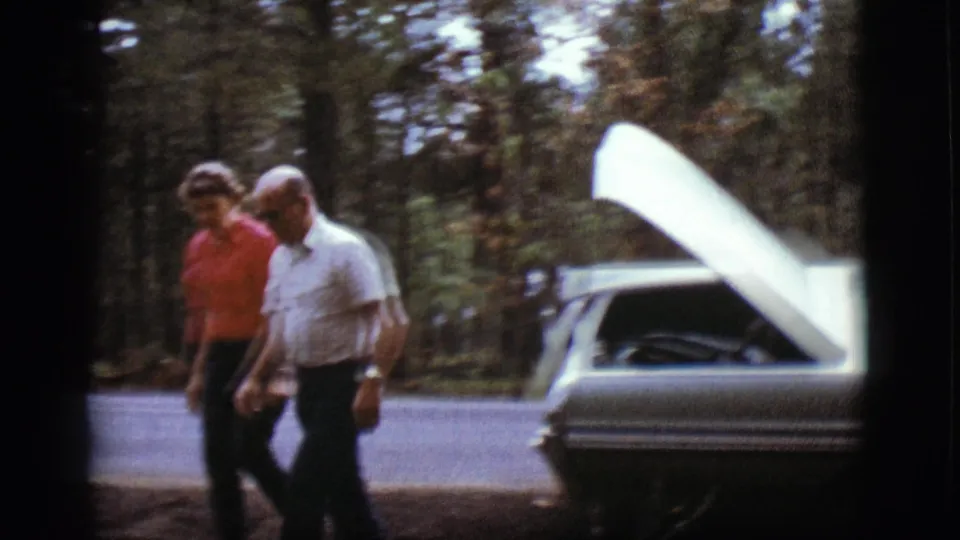 The man and woman move away from the open-hood car on the wooded roadside in the 1968 Flagstaff home-movie scene.