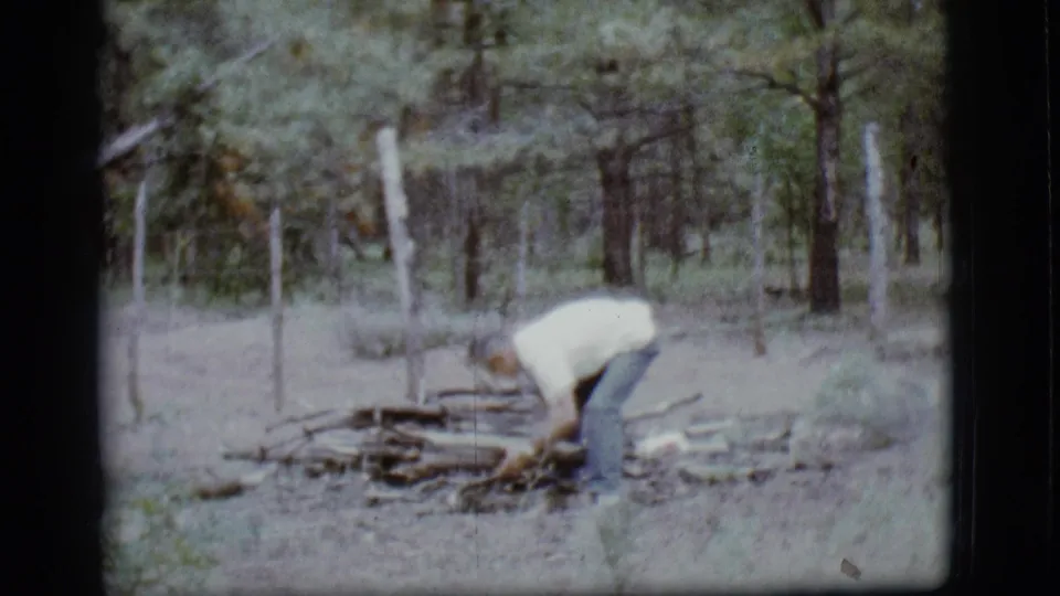 Adult man bends near a small pile of branches in the woods during the Flagstaff, Arizona home movie scene.