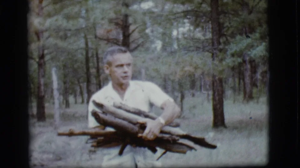 In the final frame, the man carries firewood close to the camera in the Flagstaff woods, with his face turned slightly to one side.