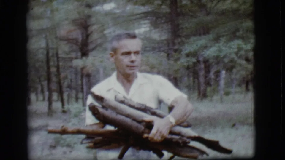 In 1968 Flagstaff home-movie footage, a man in a white short-sleeved shirt carries firewood through a pine forest.