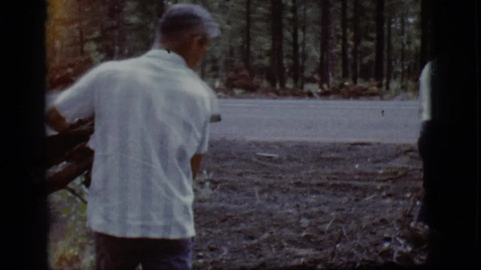 Rear view shows the man carrying firewood across a wooded clearing in the supplied Flagstaff, Arizona home-movie context.