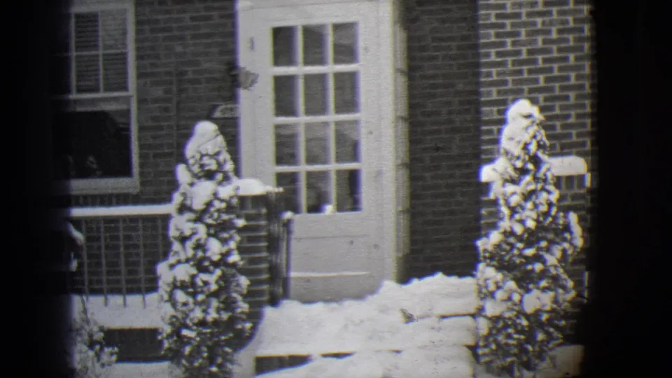 1944 Buffalo residential winter frame with a white door, brick facade, porch railing, and heavy snow on shrubs and ground.