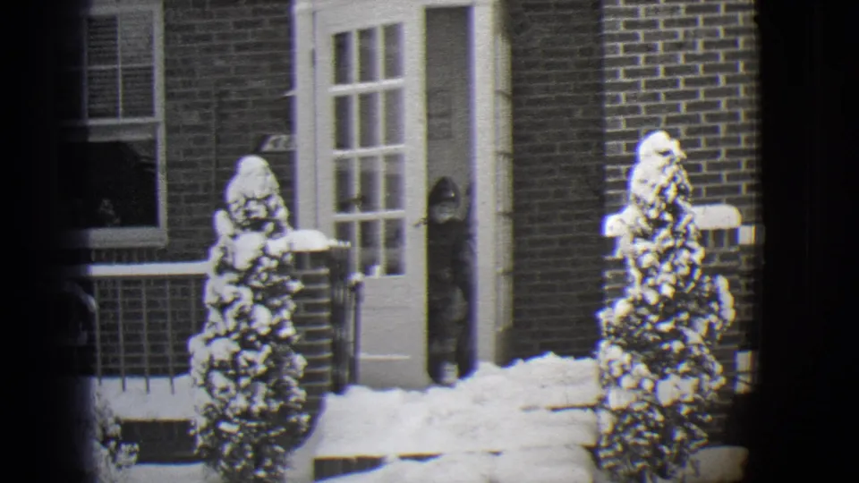 1944 Buffalo home-movie frame showing a bundled person by a white door on a snow-covered brick house porch.