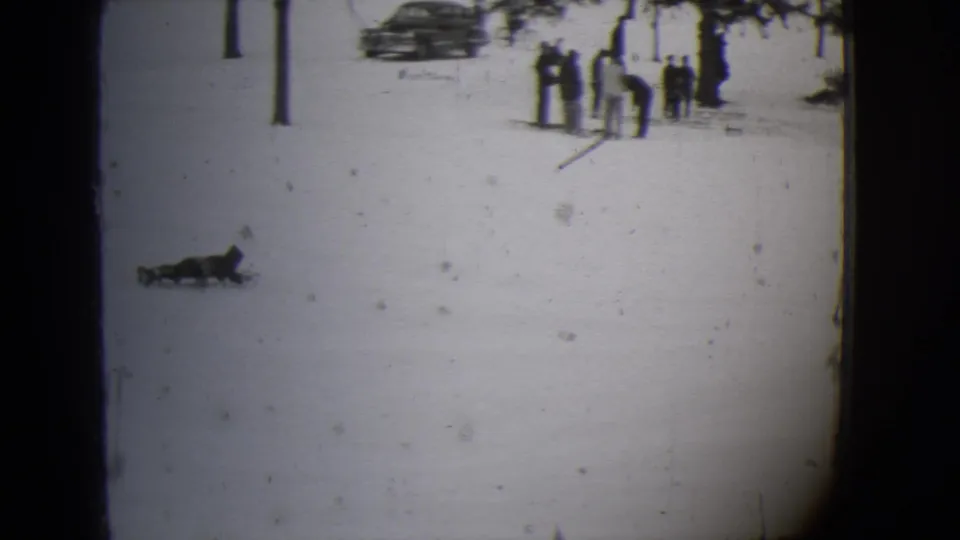 A child on a sled crosses the snow as distant people and parked cars become visible in the 1944 Buffalo footage.