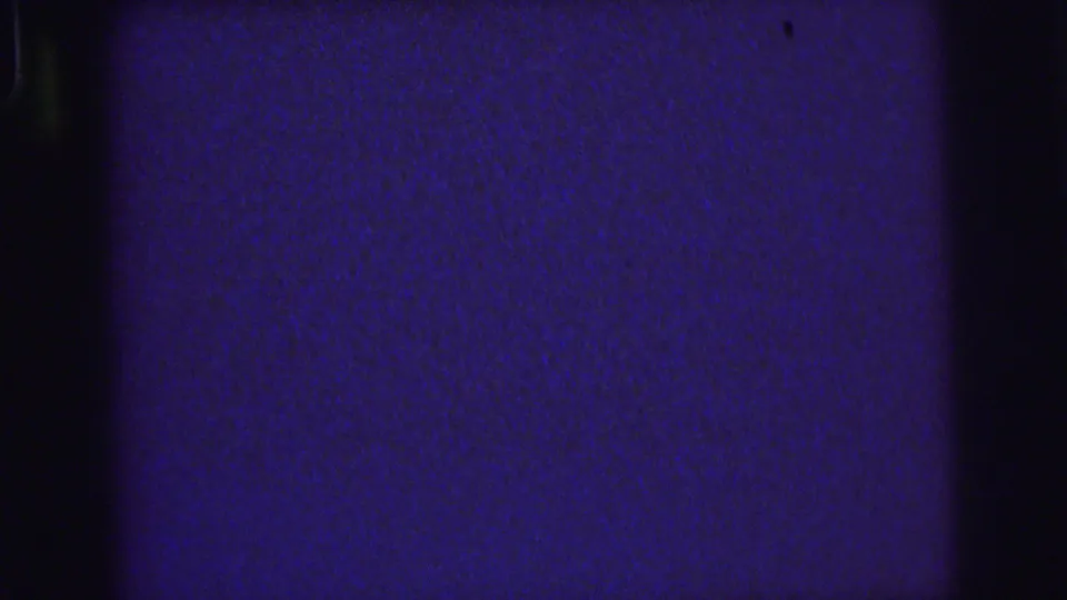 1976 Lynbrook 8mm frame showing a dark blue analog field with grain, shadowed edges, and small dust or scratch marks.