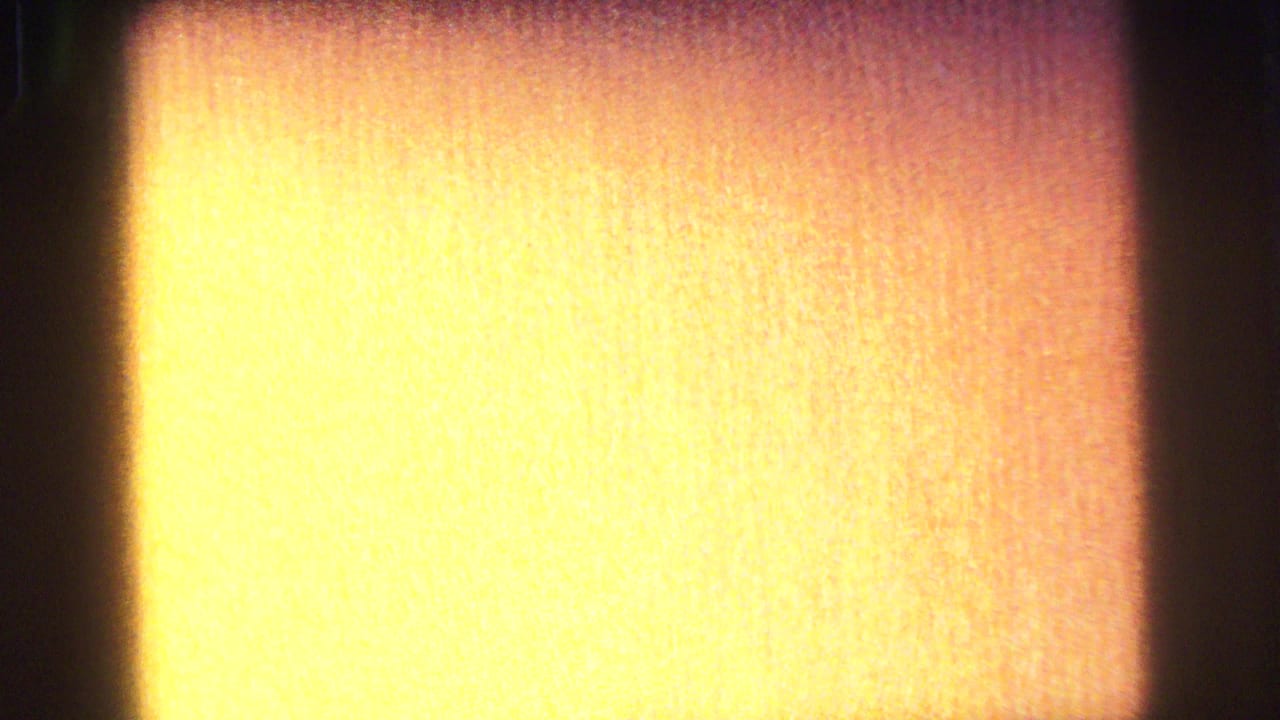 Abstract 8mm frame with bright yellow-orange exposure, dark edge falloff, and visible analog film grain.