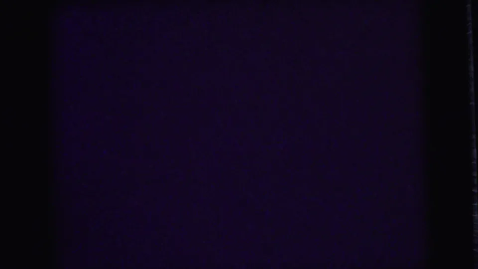 Underexposed 8mm frame from the clip with mostly dark interior space and minimal readable detail.