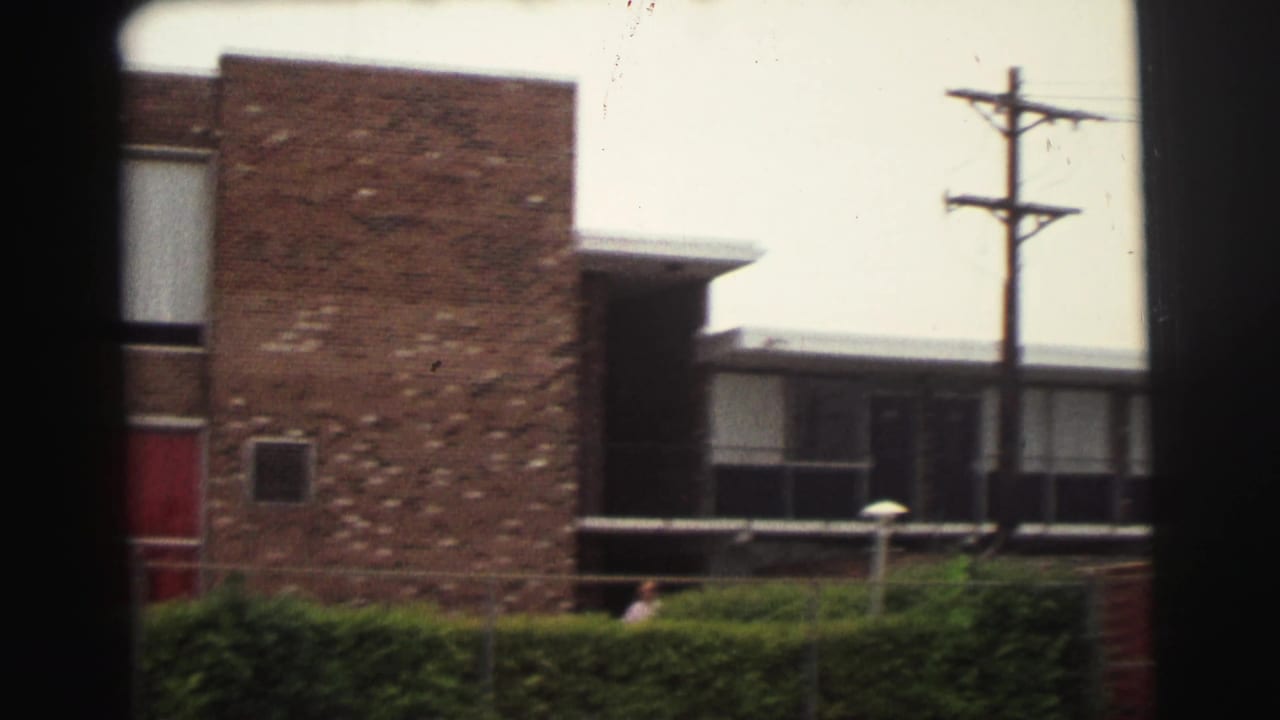 Brick motel building with a red door, hedges, utility pole, and dark film-frame borders.