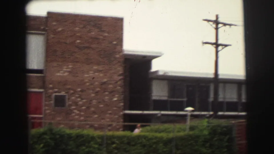 1971 Yellowstone-area home-movie frame showing a brick motel exterior, red door, hedges, and utility pole seen through dark 8mm frame edges.