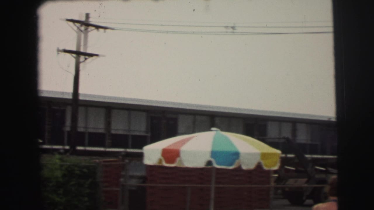 1971 Yellowstone-area resort view with a low motel block, overhead utility lines, and a multicolor patio umbrella in the foreground.