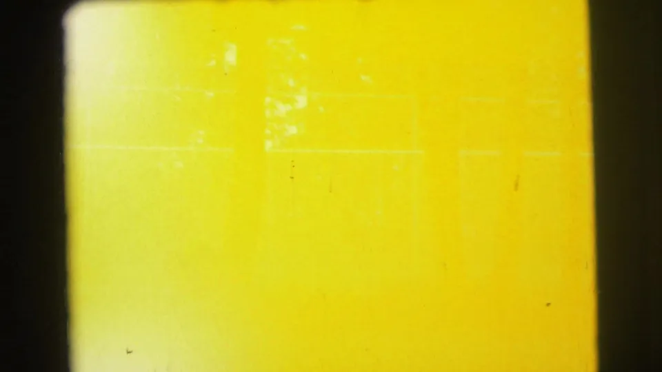 Overexposed 8mm frame from the Yellowstone clip, with faint tree and fence traces under a broad yellow wash.