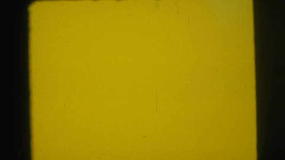 Yellow-green overexposed 8mm frame with dark film edges, grain, and small dust marks, with no distinct subject visible.