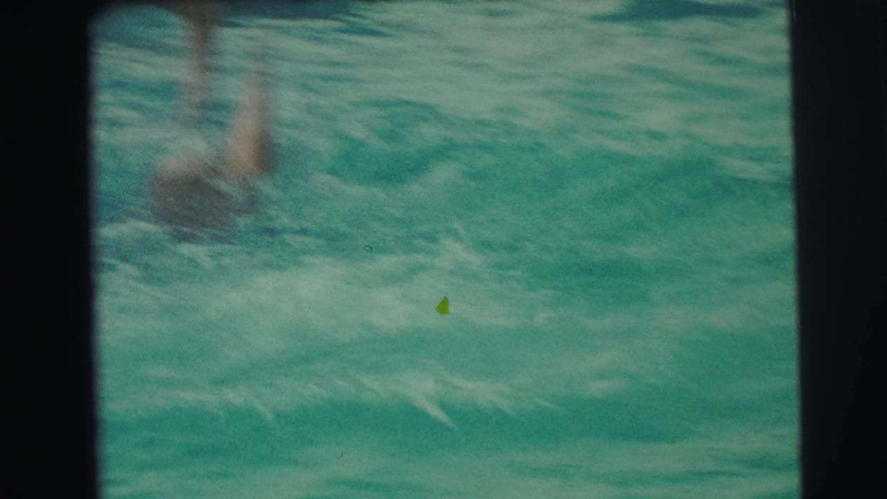 Swimmer's legs splash into turquoise pool water near a dark film border.