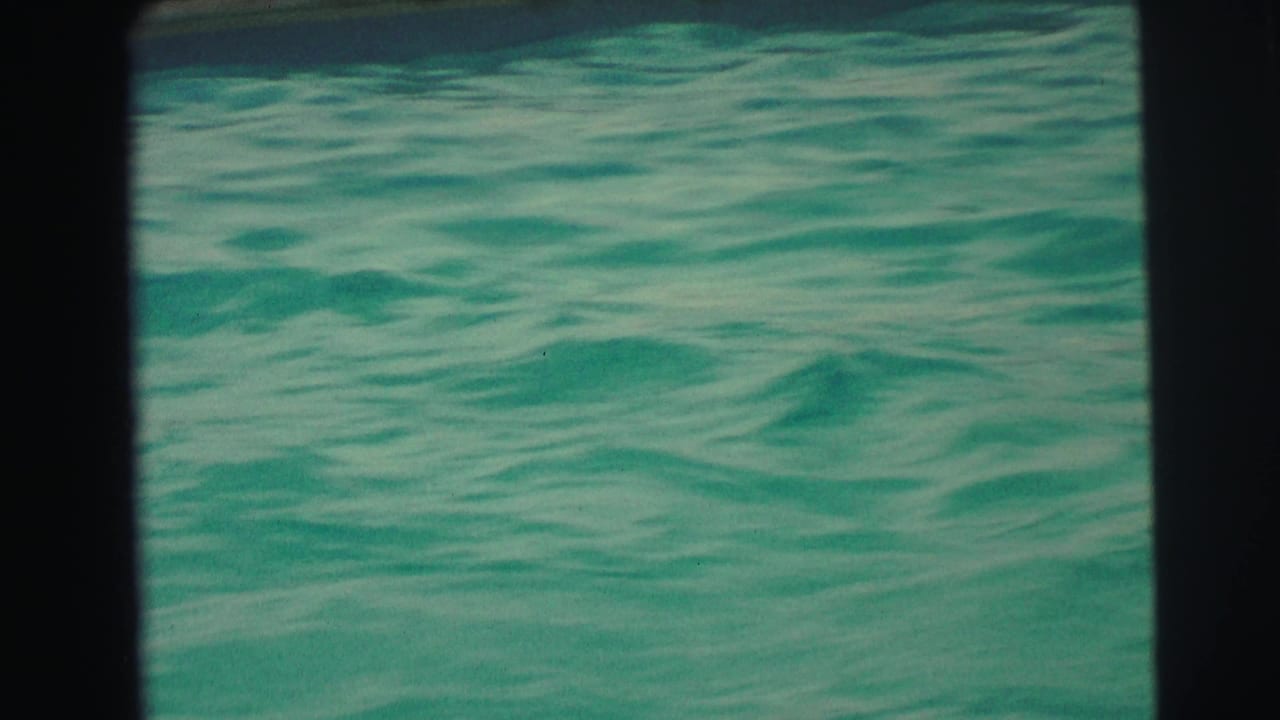 1971 Yellowstone, Wyoming home-movie frame showing only rippled turquoise pool water within dark 8mm scan borders.
